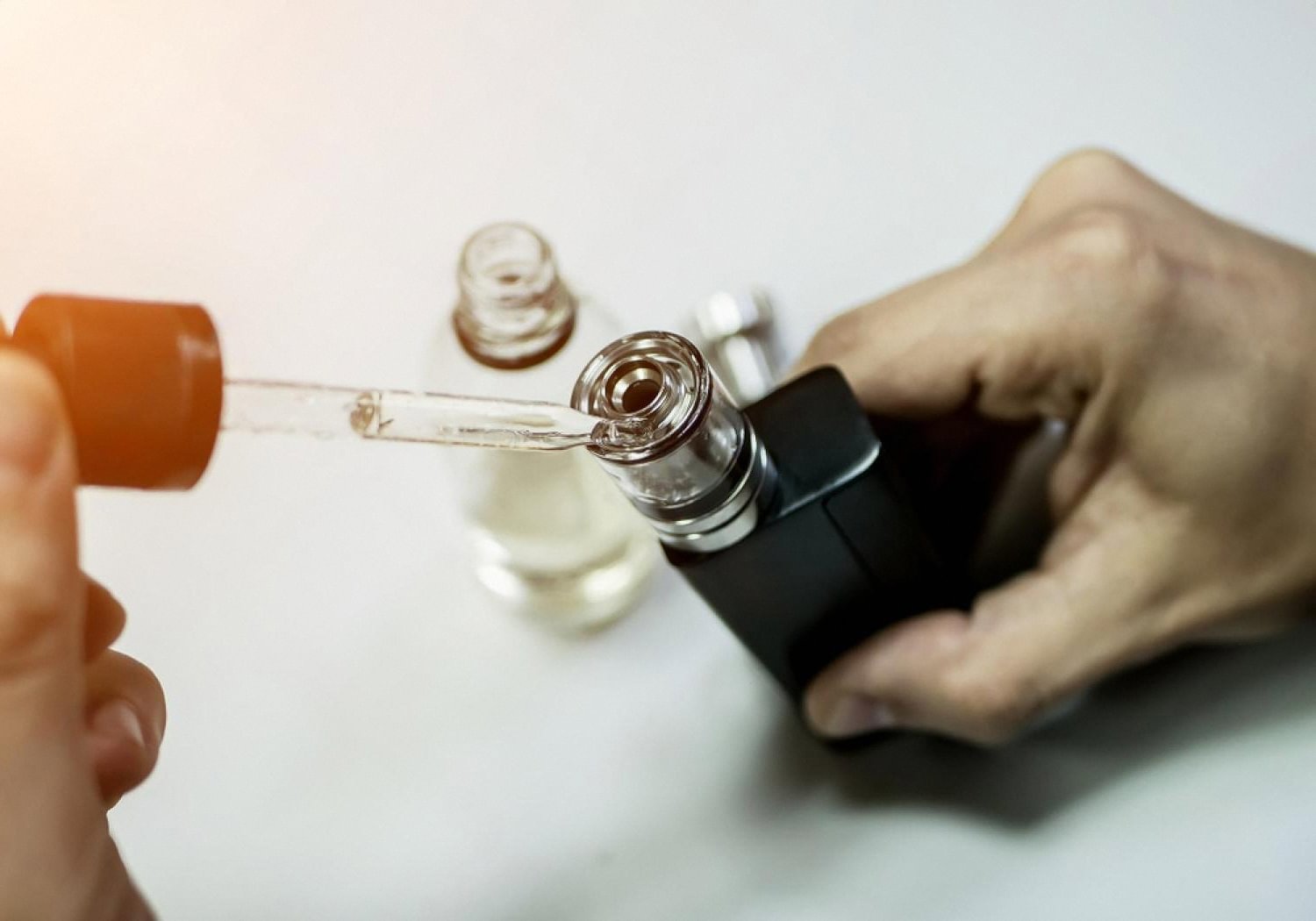 Person refilling an open-system vape mod with e-liquid using a dropper
